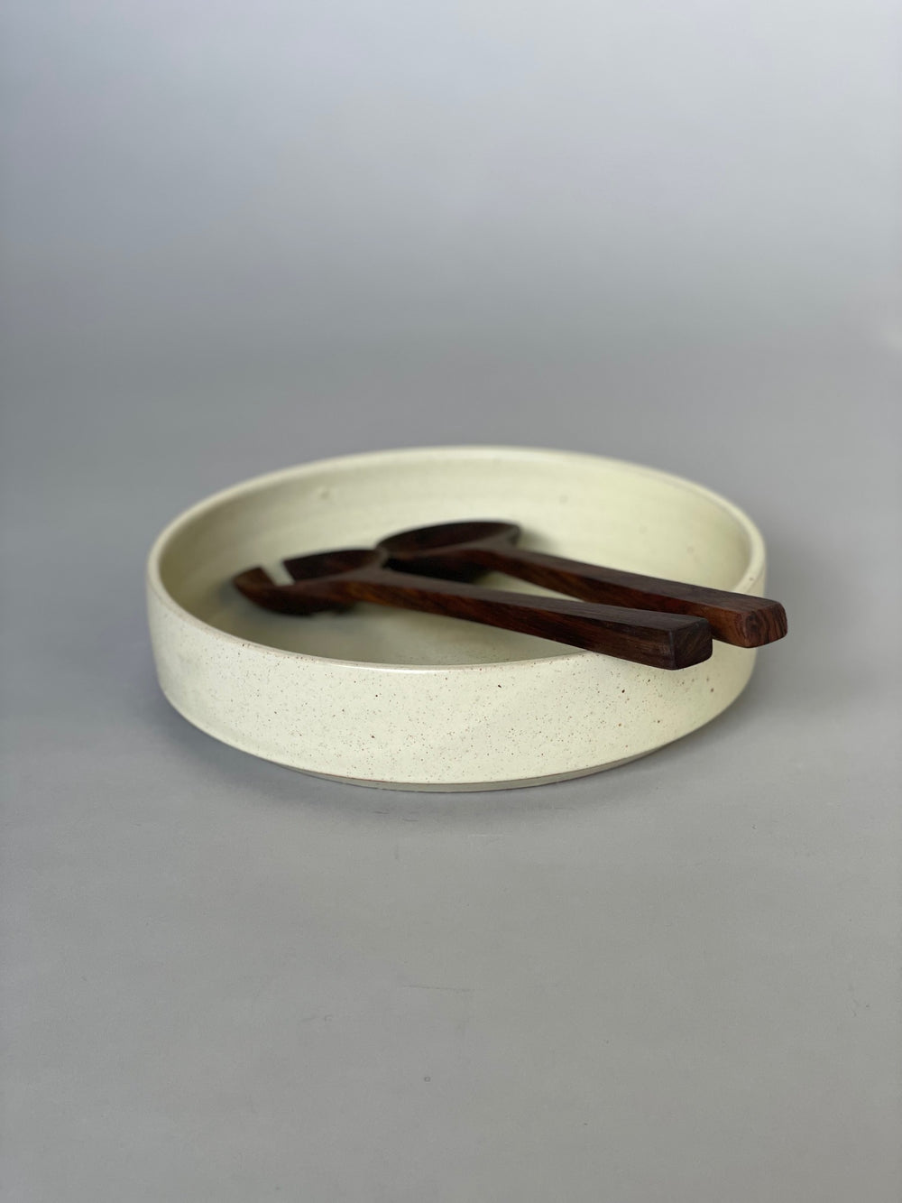 Handmade ceramic serving bowl with a soft warm white glaze, paired with walnut salad servers.