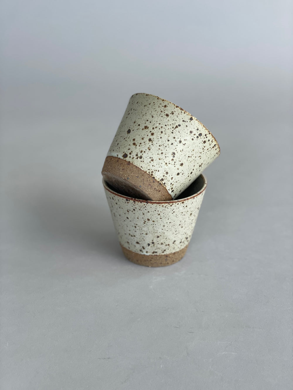 Close-up of two ceramic tumblers stacked neatly, highlighting the speckled stoneware finish.