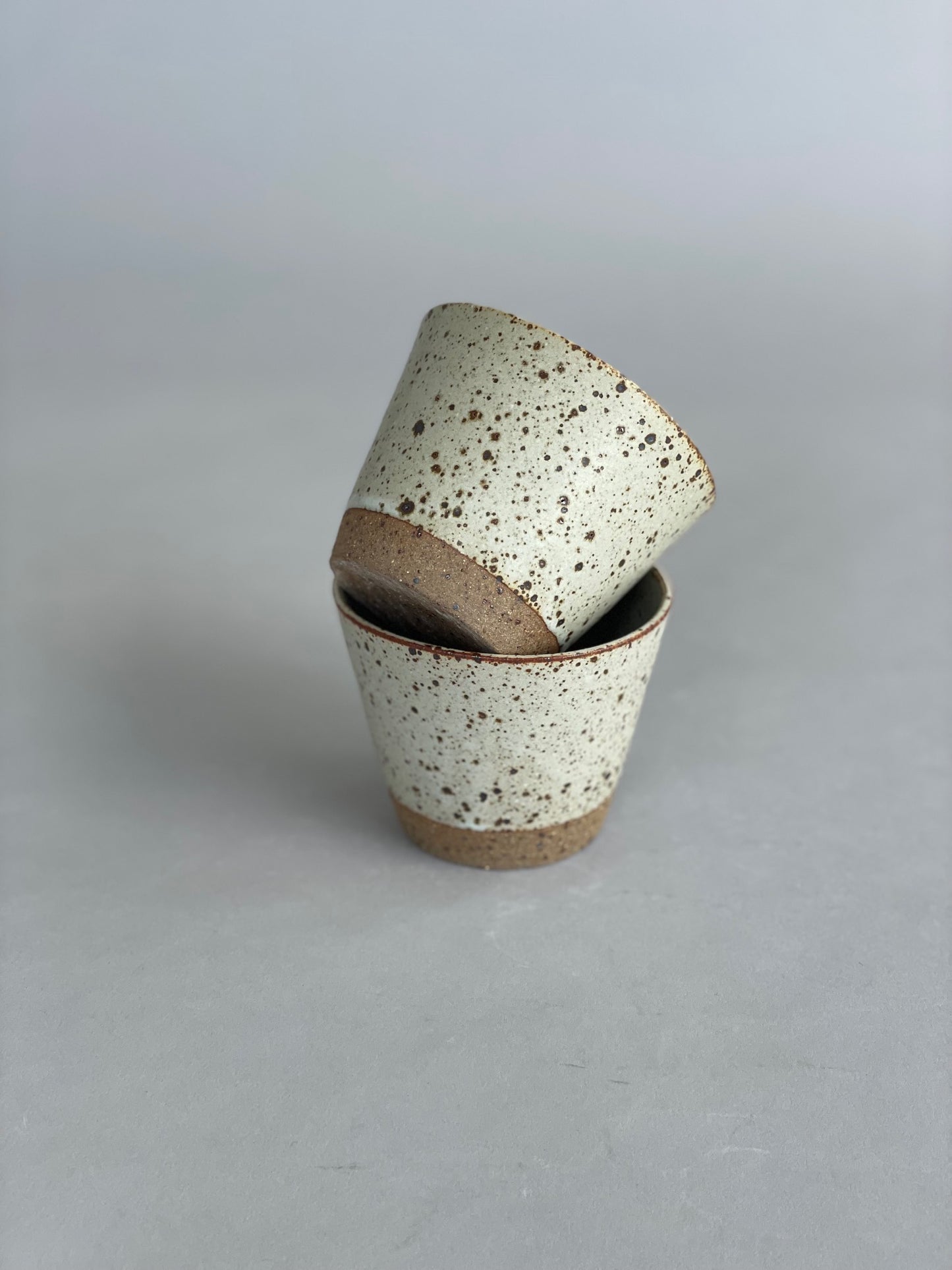 Close-up of two ceramic tumblers stacked neatly, highlighting the speckled stoneware finish.