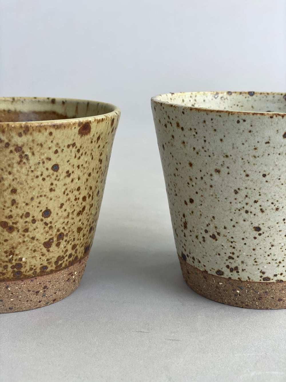Close-up of two ceramic tumblers side by side, highlighting the speckled stoneware finish.