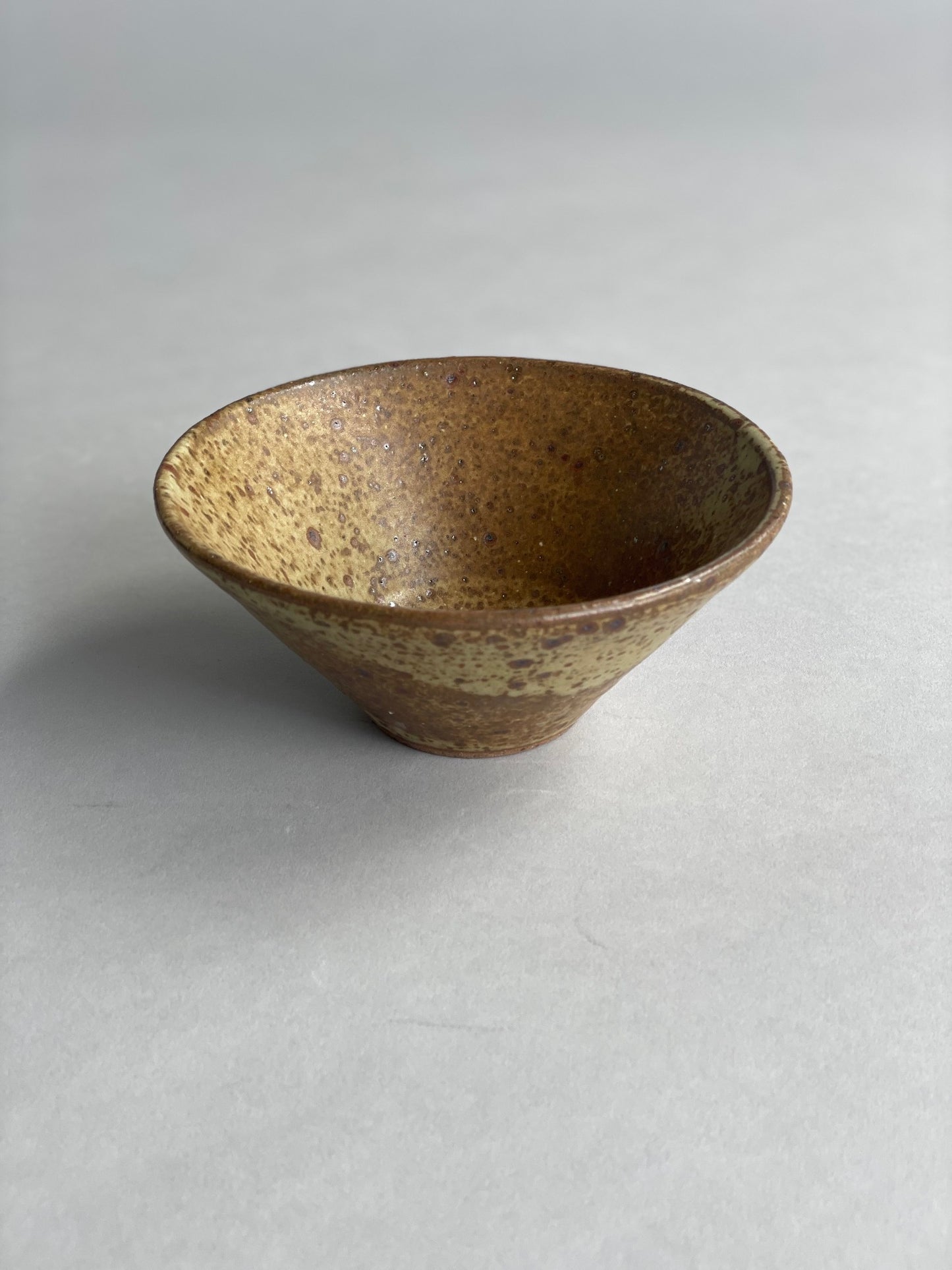 Speckled ceramic bowl on a neutral surface, showcasing its natural stoneware texture and warm glaze.
