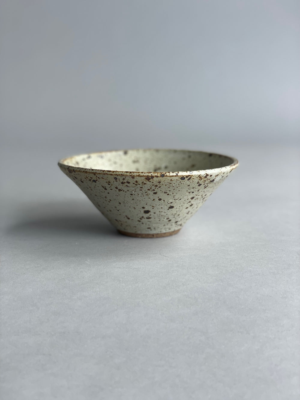 Single handmade ceramic bowl with a speckled glaze, highlighting its minimalist design and smooth finish.