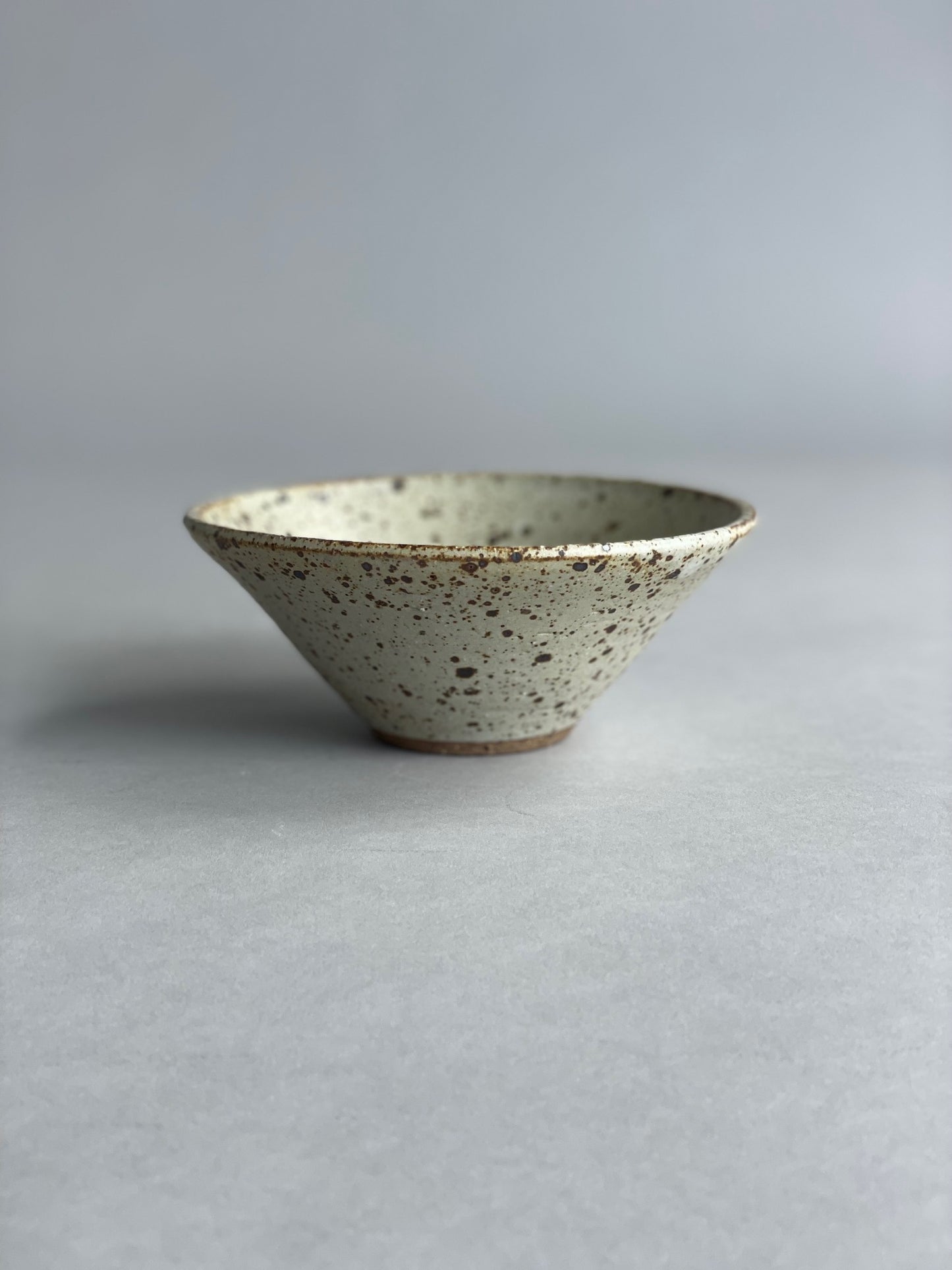 Single handmade ceramic bowl with a speckled glaze, highlighting its minimalist design and smooth finish.
