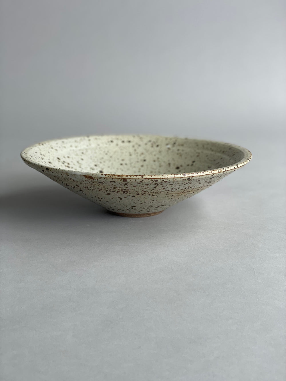 Handmade ceramic bowl with a warm speckled glaze, showcasing a simple and modern design.