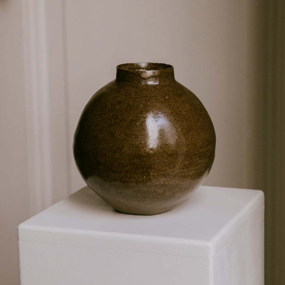 Stoneware vase resting on a minimalist surface, showing the interplay of its warm glaze and dark clay.