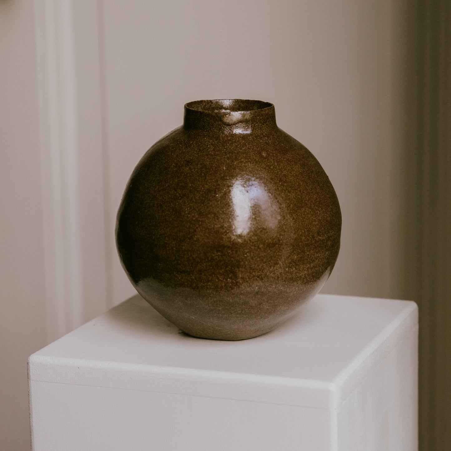 Stoneware vase resting on a minimalist surface, showing the interplay of its warm glaze and dark clay.