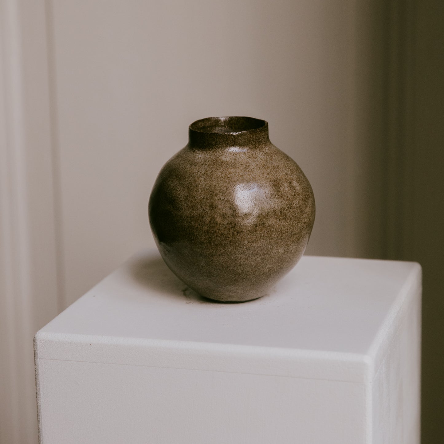 Stoneware vase resting on a minimalist surface, showing the interplay of its warm glaze and dark clay.