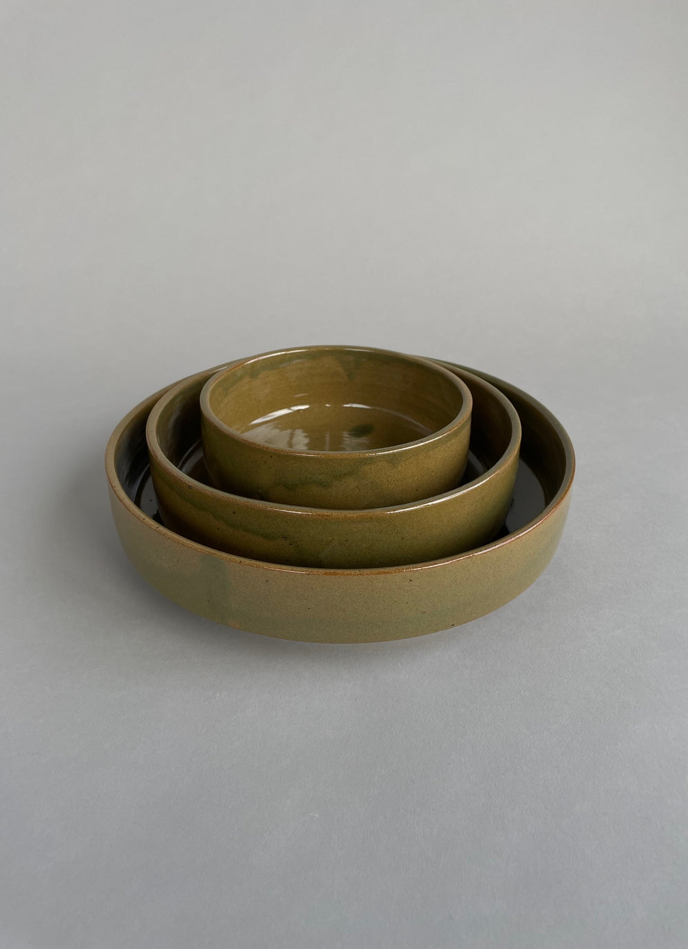 Set of three handmade nesting bowls with a warm green glaze and speckled clay finish.