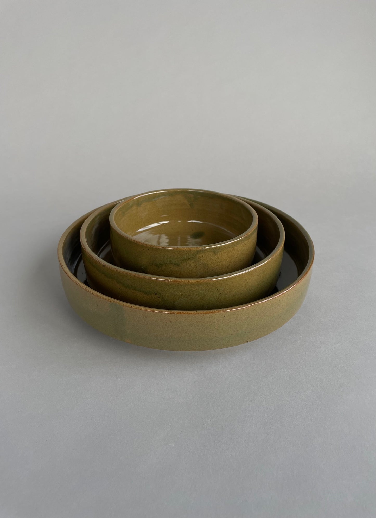 Set of three handmade nesting bowls with a warm green glaze and speckled clay finish.
