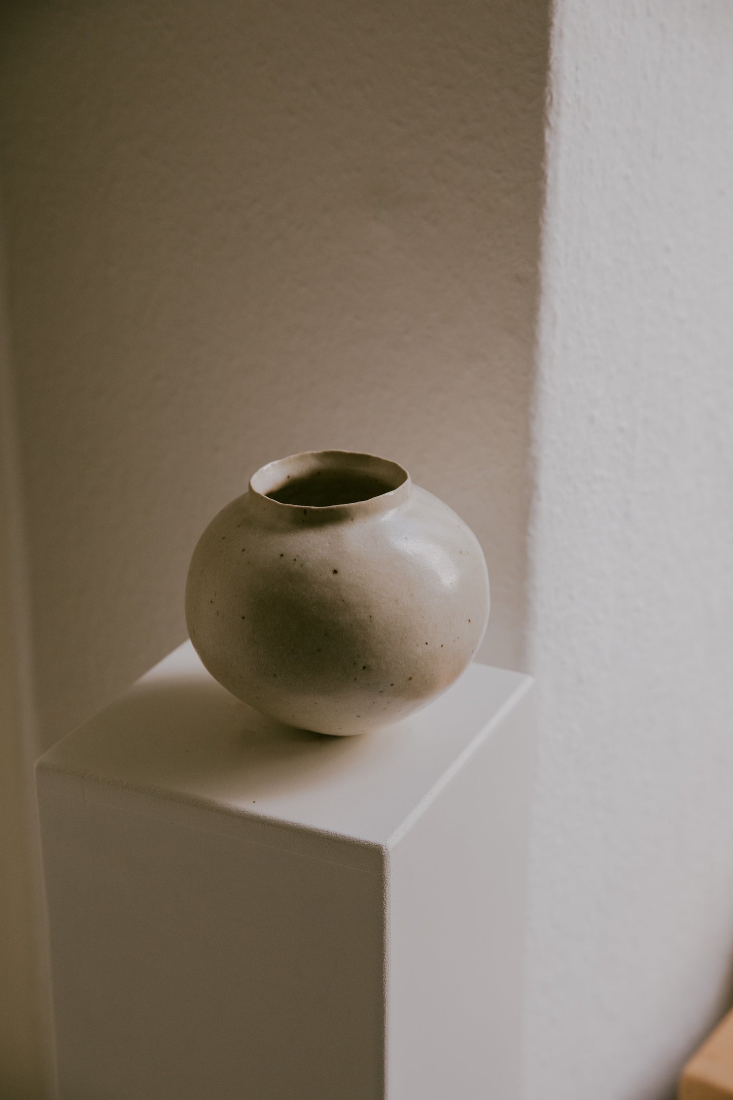 Stoneware vase resting on a minimalist surface, showing the interplay of its warm glaze and light clay.
