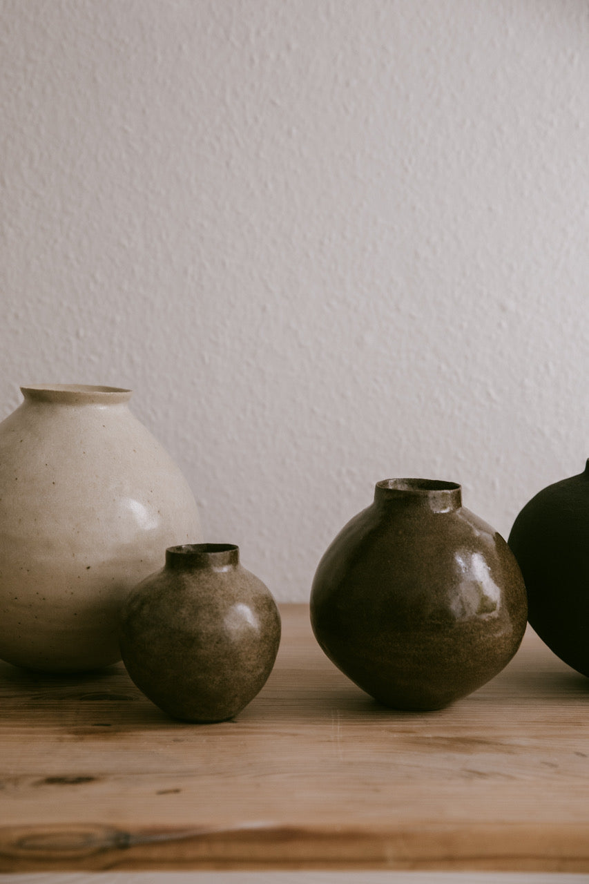 Group of handmade ceramic vases by Tor Harrison displayed on a wooden table, showcasing their earthy glazes and organic forms.
