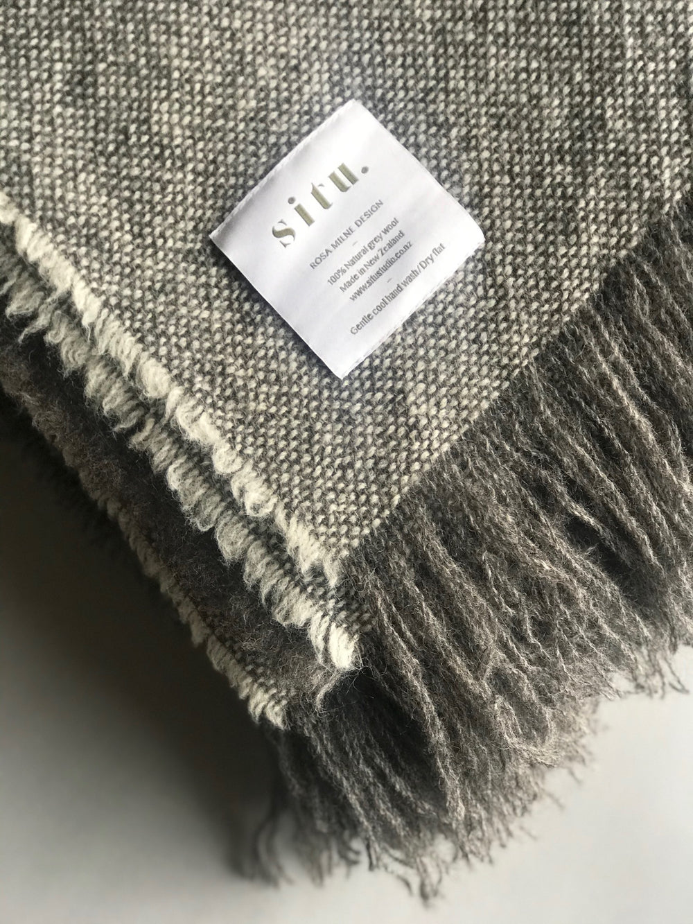 Close-up of the folded edges of the Situ wool blanket, highlighting the natural untreated grey and ecru hues and soft textured weave.