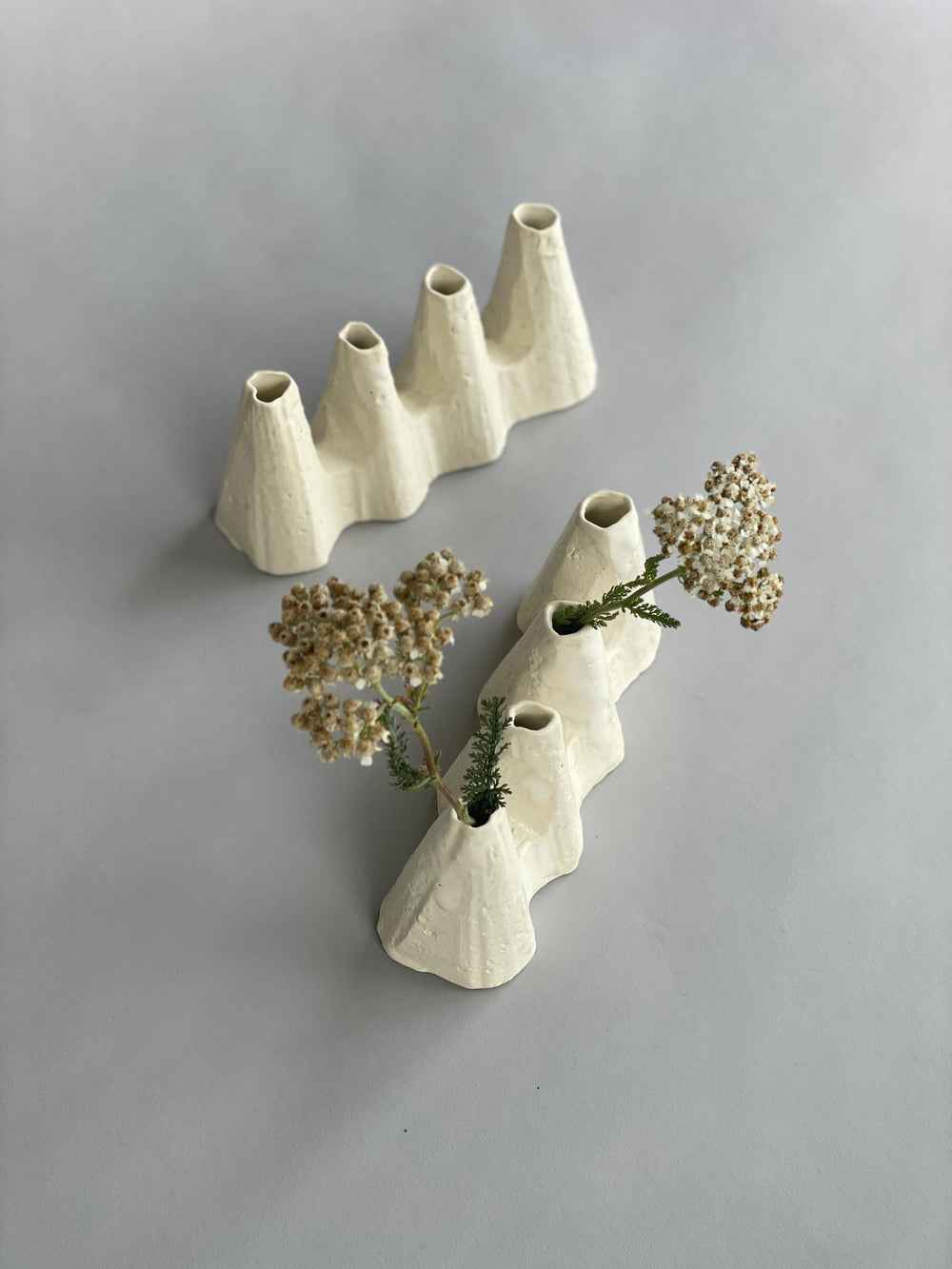 Two sculptural white ceramic vases made by artist Kirsten Perry, one with flowers in