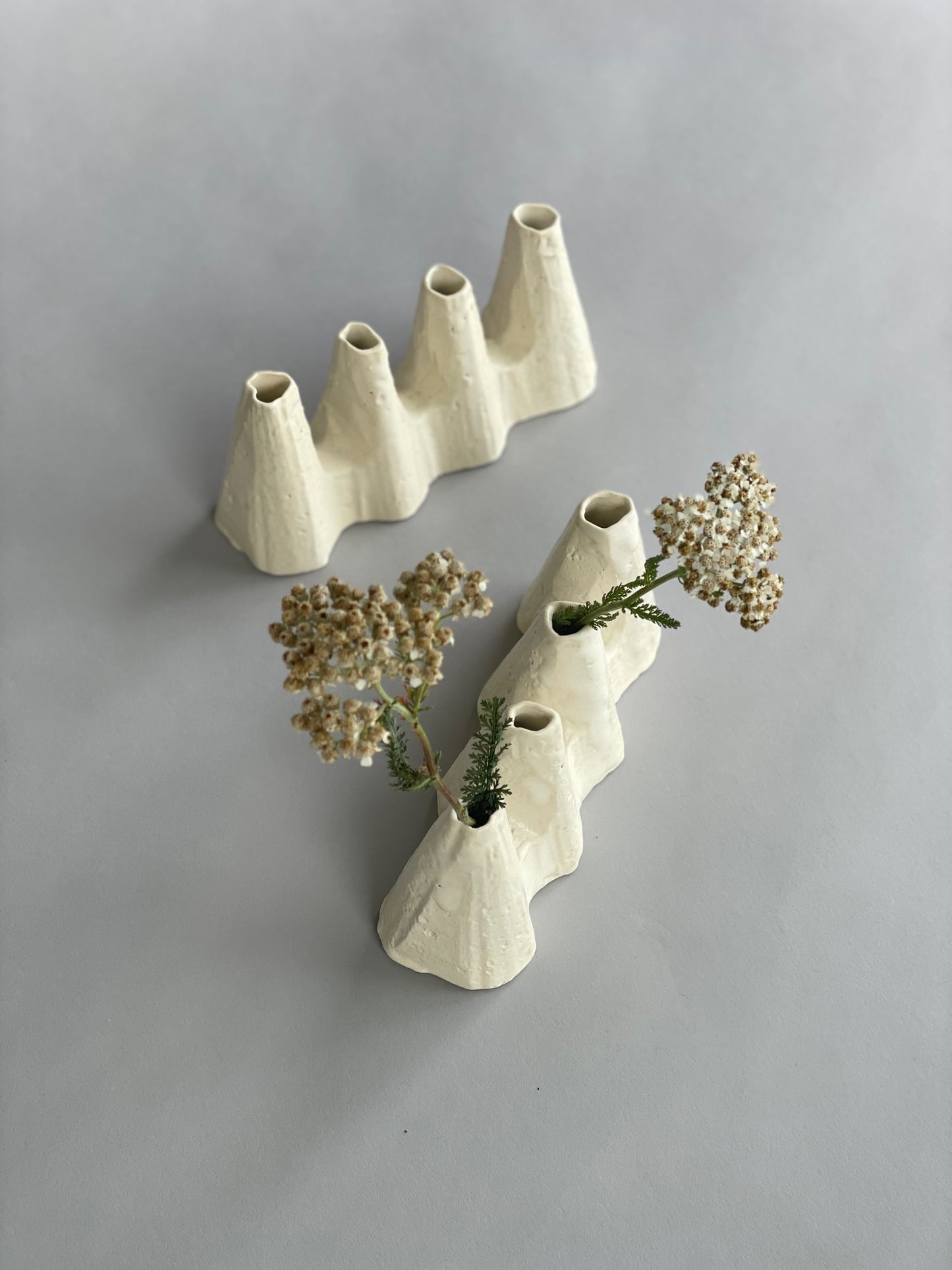Two sculptural white ceramic vases made by artist Kirsten Perry, one with flowers in