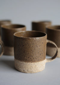 Handcrafted stoneware cup with a warm speckled surface and a muddy green matte glaze.