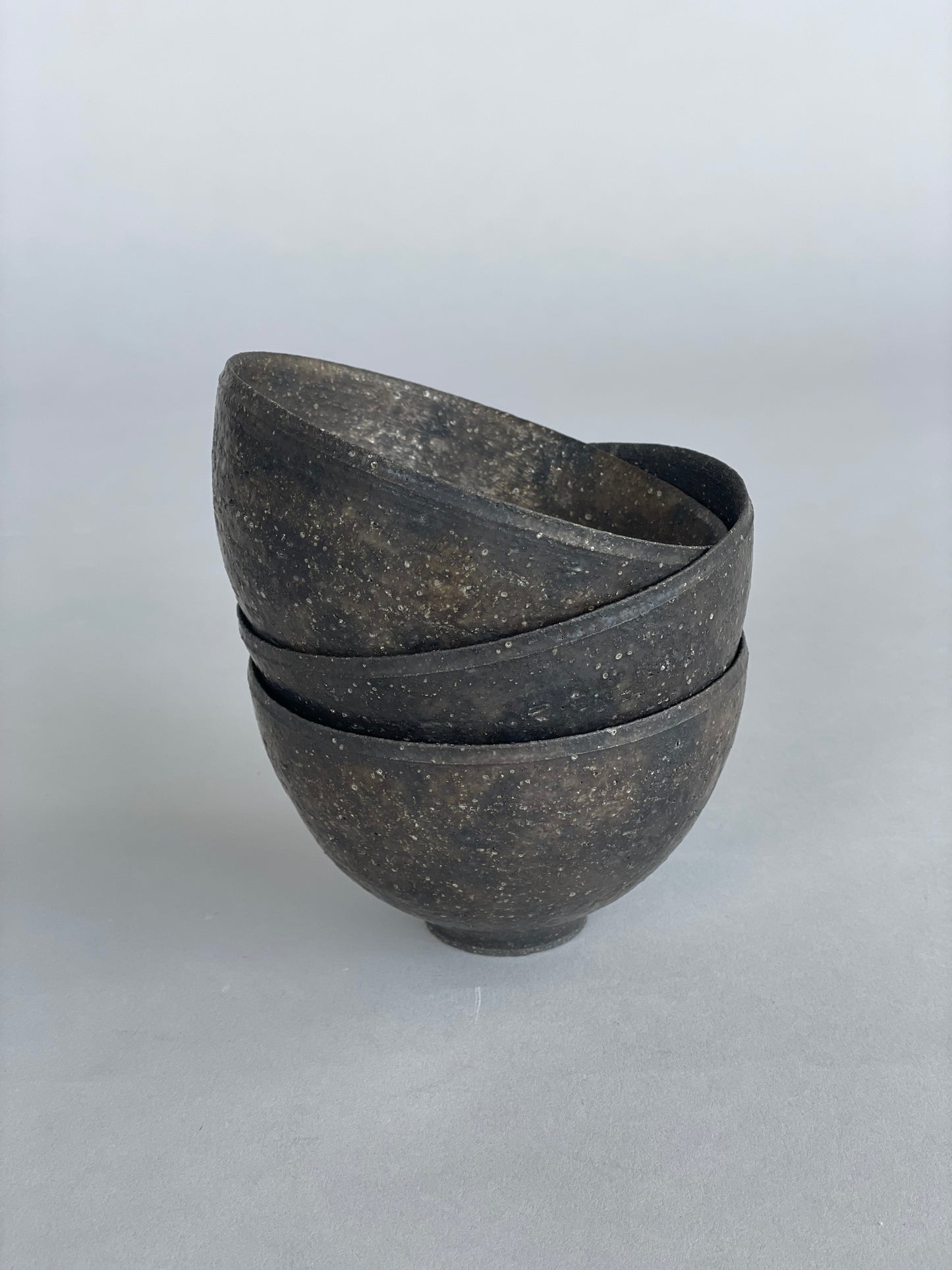 A stack of three handmade ceramic rice bowls. Made by Takashi Endo in a textural  black glaze.