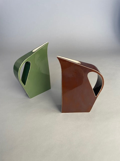 Two Yuro Cuchor handmade jugs in rich brown glaze placed side by side on a neutral surface, highlighting their contemporary geometric forms and subtle glaze variations.