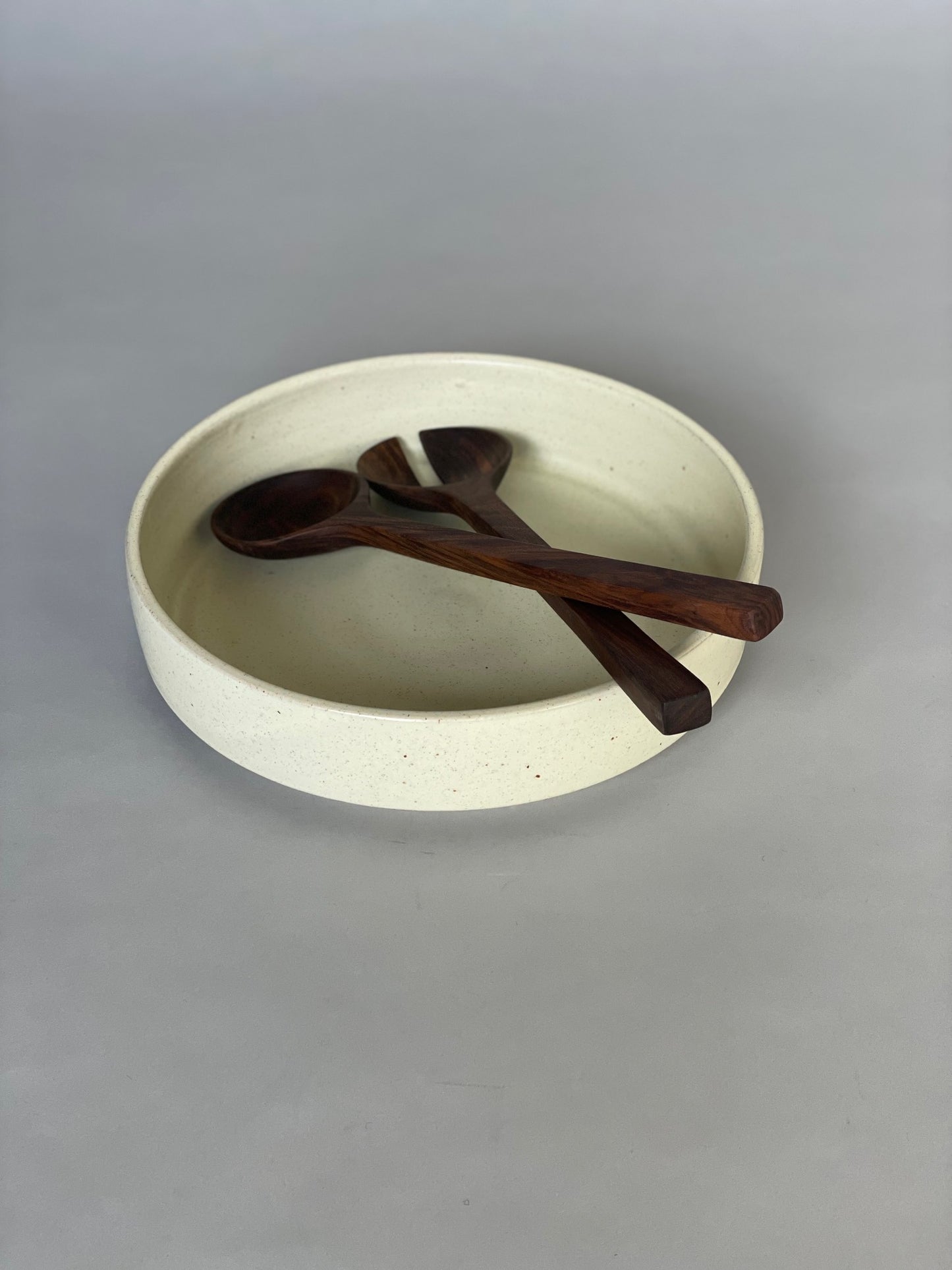 Handmade ceramic serving bowl with a soft warm white glaze, paired with walnut salad servers.