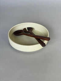 Handmade ceramic serving bowl with a soft warm white glaze, paired with walnut salad servers.