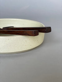 Walnut salad servers resting inside a ceramic bowl, showcasing their hand-carved craftsmanship.