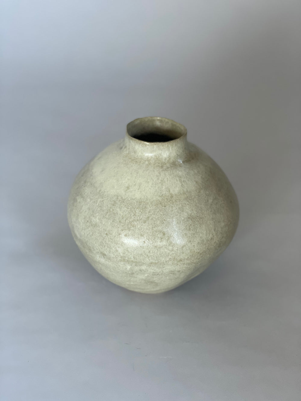 Stoneware vase resting on a minimalist surface, showing the interplay of its warm glaze and dark clay.