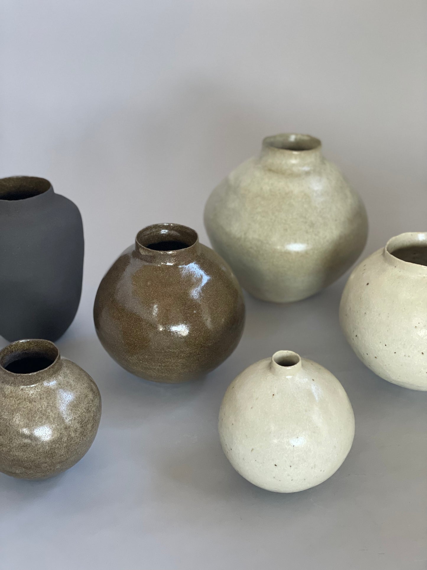 Group of handmade ceramic vases by Tor Harrison displayed on a minimalist surface, showcasing their earthy glazes and organic forms.