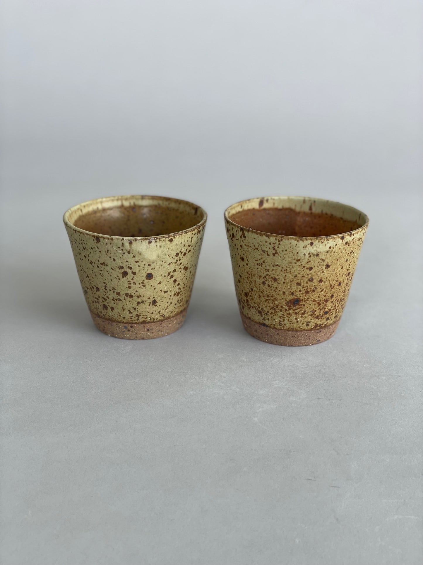 Close-up of two ceramic tumblers stacked neatly, highlighting the speckled stoneware finish.