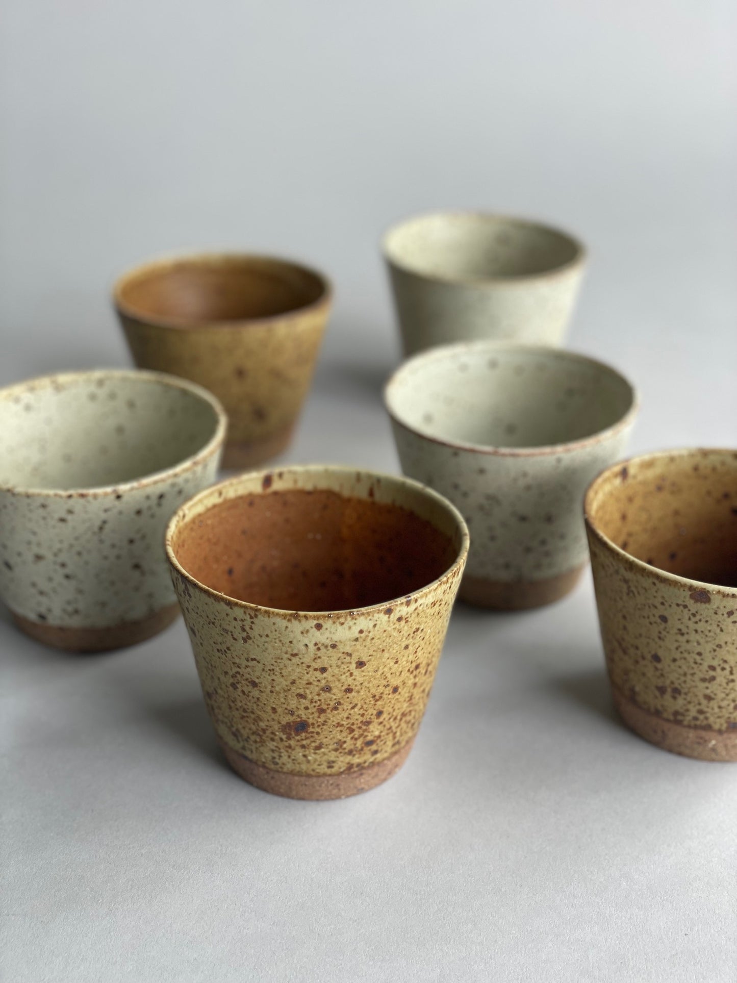 A group of handmade ceramic tumblers arranged side by side, showing variations in size and glaze.