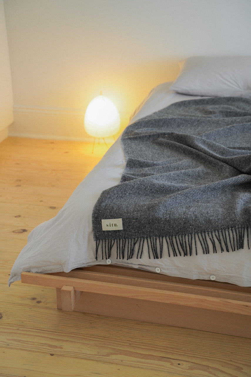 Handwoven wool blanket draped over a bed, highlighting its generous size and textured design.