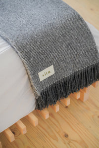 Handwoven wool blanket draped over a bed, highlighting its generous size and textured design.