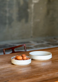 Two ceramic bowls grouped together on a dining table, highlighting their soft white glaze and modern proportions.