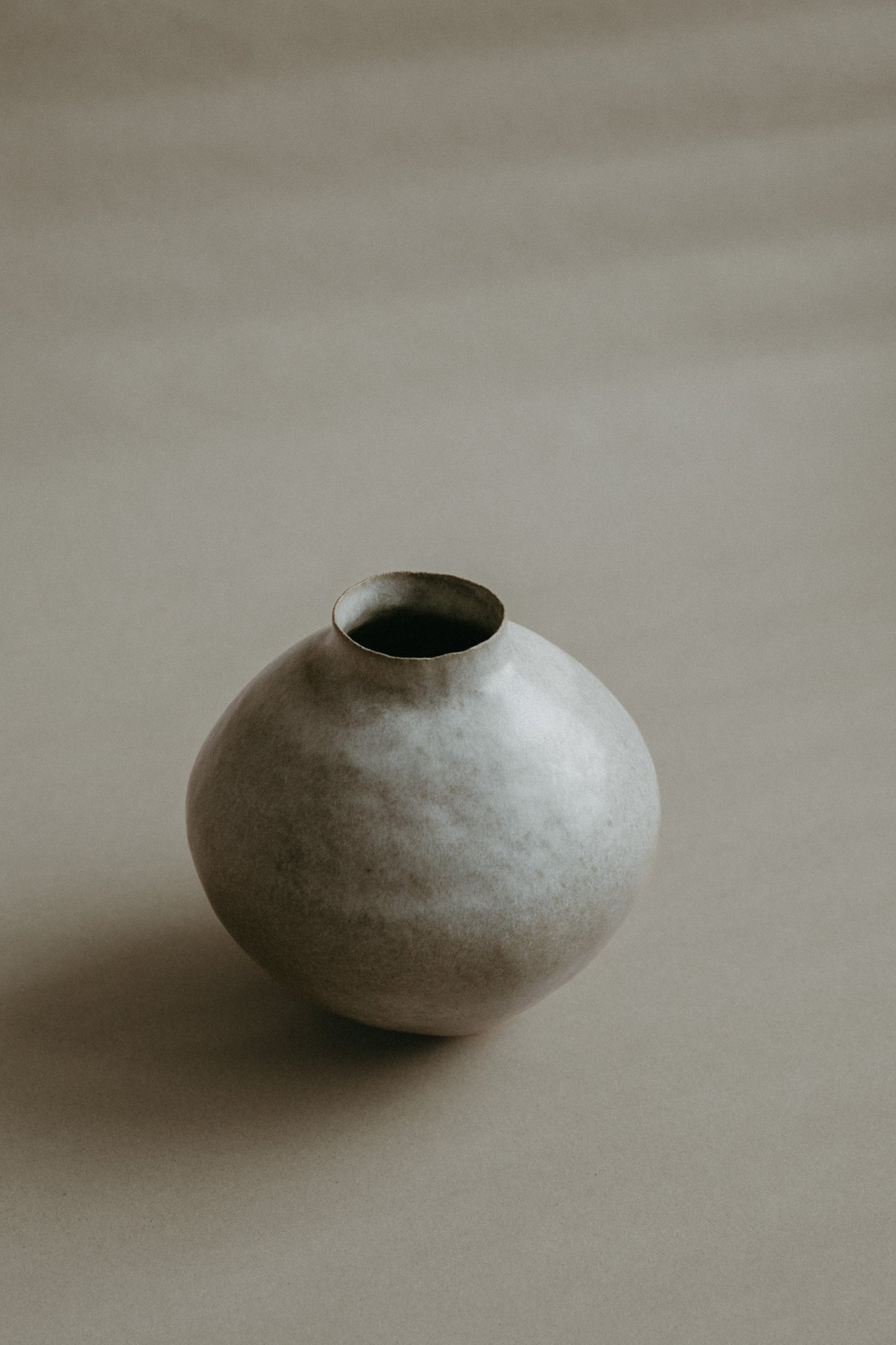 Stoneware vase resting on a minimalist surface, showing the interplay of its warm glaze and dark clay.