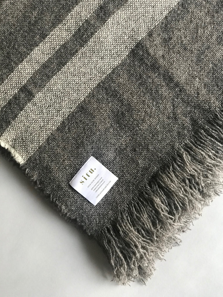 Soft luxurious wool throw made in New Zealand and designed by Situ Studio. A natural dark grey with an ecru stripe making this blanket a classic to style your home with. Made to last and to use everyday.