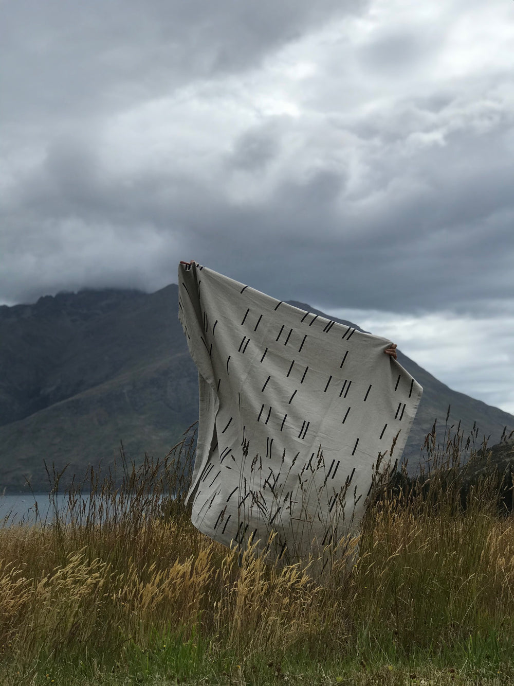 Person holding up a Modern Geometry linen throw against a natural backdrop, showcasing its geometric design and raw selvedge edges.