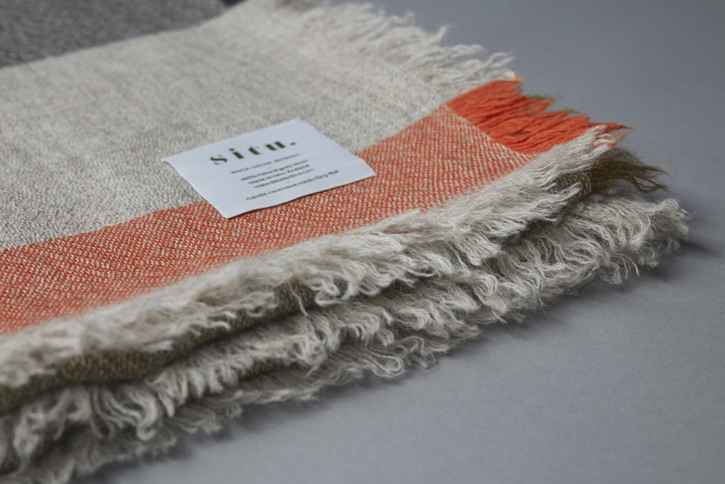 Lightweight and soft wool blanket made in New Zealand and designed by Situ Studio. A light grey wool with intermittent stripes of Olive Green, Charcoal and orange.